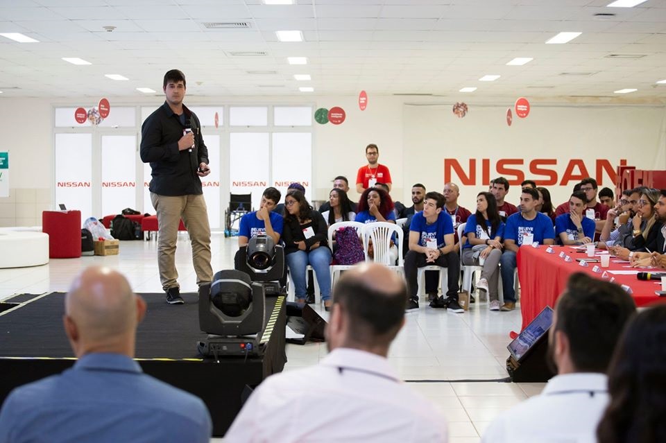 apresentação de aluno no palco da Nissan. ao fundo, participantes estão sentados, ao redor do palco 